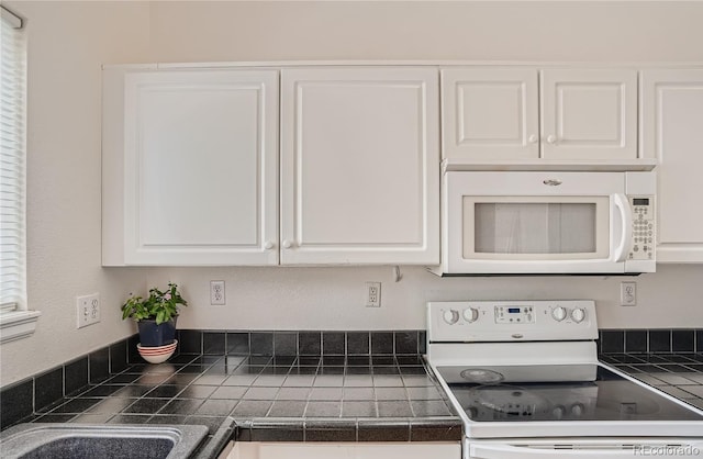 kitchen with white appliances, white cabinetry, and tile counters