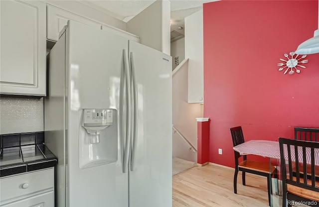 kitchen featuring white refrigerator with ice dispenser, light wood finished floors, and white cabinetry