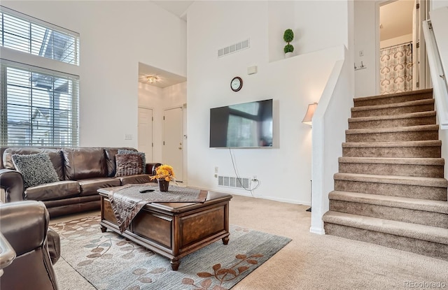 carpeted living room with a towering ceiling, stairway, and baseboards