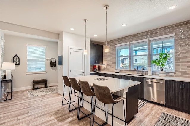 kitchen featuring dishwasher, sink, hanging light fixtures, light hardwood / wood-style flooring, and a breakfast bar area