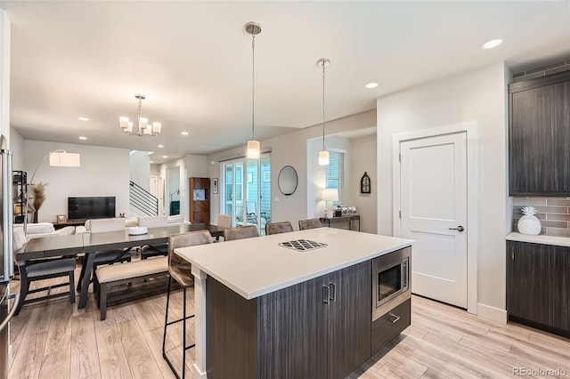 kitchen with pendant lighting, a kitchen island, stainless steel microwave, and light wood-type flooring