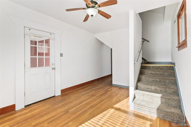 entryway with stairs, wood finished floors, a ceiling fan, and baseboards