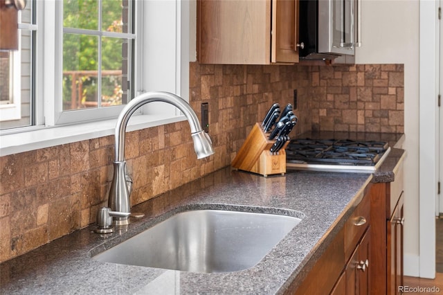8029 E 23rd Ave, Denver, CO 80238 - kitchen view of a sink, brown cabinetry, backsplash, stainless steel gas cooktop, and dark countertops