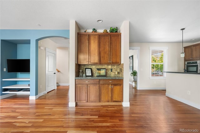 8029 E 23rd Ave, Denver, CO 80238 - kitchen featuring stainless steel oven, light wood-type flooring, arched walkways, dark countertops, and brown cabinets