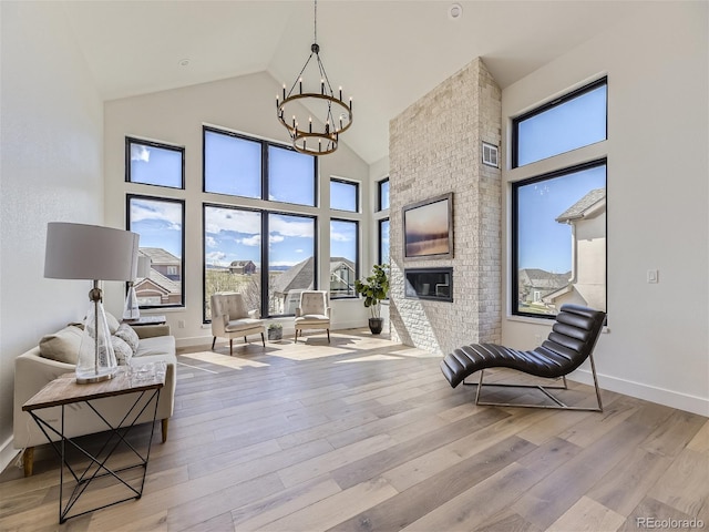 sitting room featuring a brick fireplace, light hardwood / wood-style flooring, high vaulted ceiling, and a chandelier