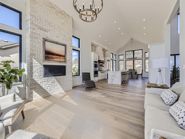 living room featuring a high ceiling, light wood-type flooring, a large fireplace, and an inviting chandelier