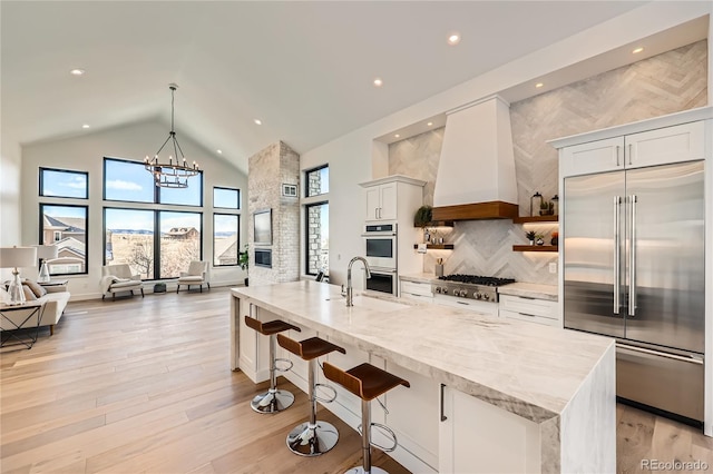 kitchen with a breakfast bar, premium range hood, white cabinets, light stone countertops, and appliances with stainless steel finishes