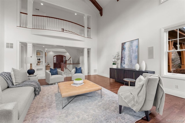 living room featuring dark wood-type flooring, high vaulted ceiling, beam ceiling, and decorative columns