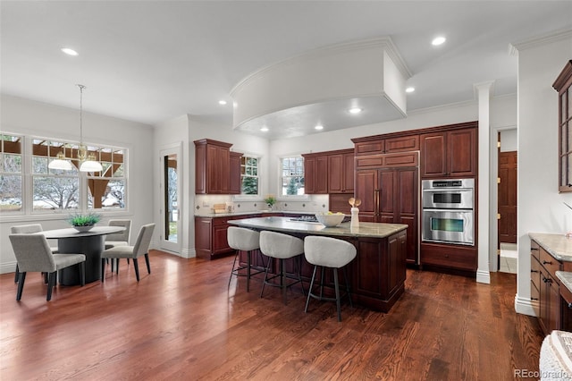 kitchen with a kitchen island, dark hardwood / wood-style floors, decorative light fixtures, light stone counters, and stainless steel double oven