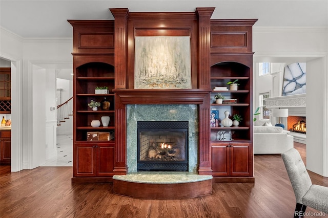 unfurnished living room with built in shelves, wood-type flooring, a fireplace, and crown molding