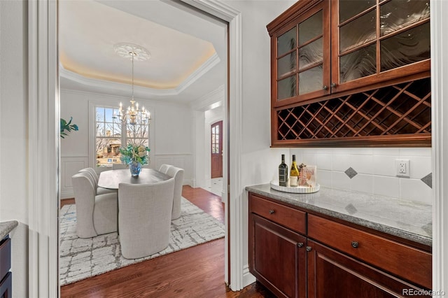 dining area with a chandelier, dark hardwood / wood-style flooring, bar, a raised ceiling, and crown molding