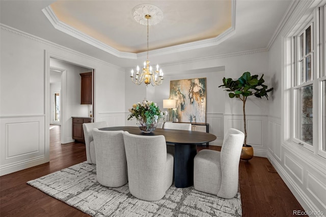 dining area featuring a raised ceiling, ornamental molding, dark wood-type flooring, and a notable chandelier