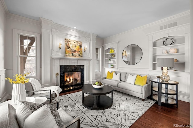 living room featuring built in shelves, wood-type flooring, ornamental molding, and a high end fireplace