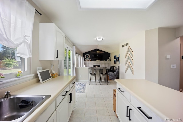 5552 S Lisbon Ln, Centennial, CO 80015 - kitchen with lofted ceiling, a brick fireplace, light tile patterned floors, white cabinets, and light countertops