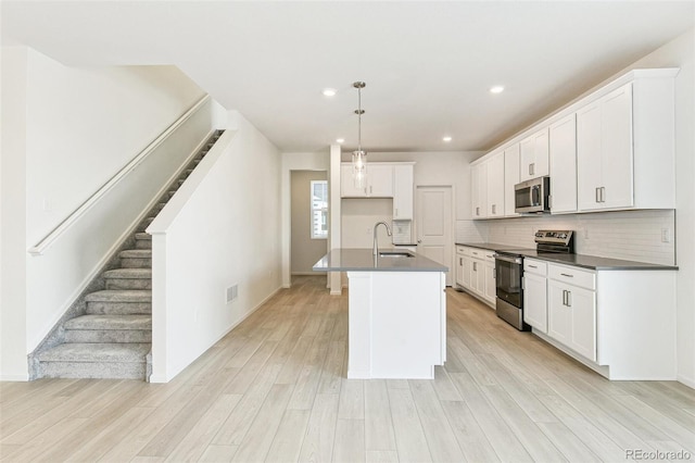 kitchen with sink, decorative light fixtures, a center island with sink, appliances with stainless steel finishes, and light wood-type flooring