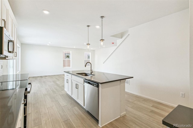 kitchen featuring appliances with stainless steel finishes, sink, a center island with sink, white cabinetry, and hanging light fixtures