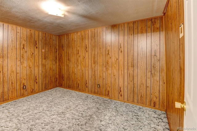 carpeted spare room featuring a textured ceiling and wooden walls