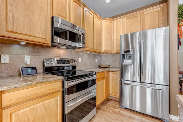 kitchen featuring light stone counters, light brown cabinetry, backsplash, and appliances with stainless steel finishes