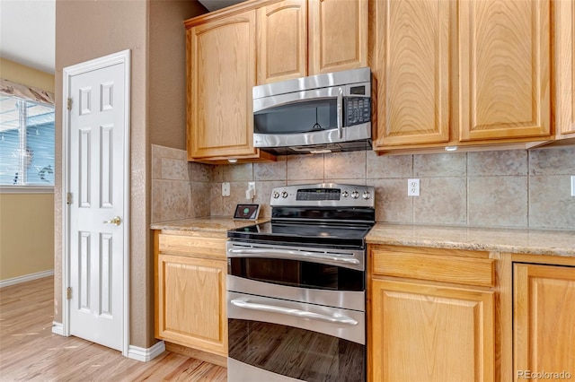 kitchen with tasteful backsplash, light brown cabinets, appliances with stainless steel finishes, light stone countertops, and light hardwood / wood-style floors