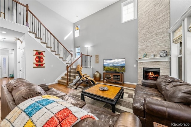 living room with wood finished floors, a towering ceiling, stairway, a fireplace, and baseboards