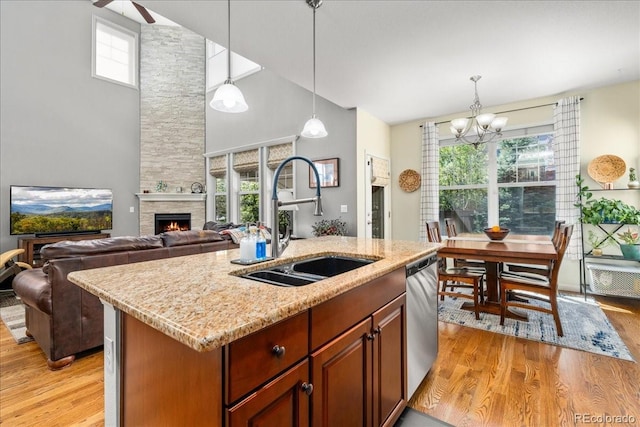 kitchen featuring an inviting chandelier, a sink, light wood-type flooring, stainless steel dishwasher, and a stone fireplace
