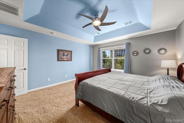carpeted bedroom with a tray ceiling, visible vents, baseboards, and ceiling fan