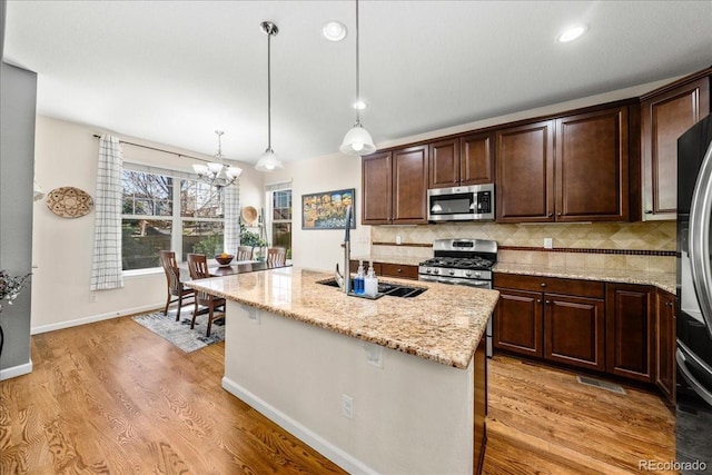 kitchen with a notable chandelier, light stone counters, dark brown cabinetry, tasteful backsplash, and appliances with stainless steel finishes