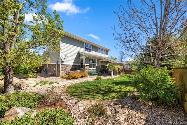 rear view of house featuring stone siding, a patio area, a lawn, and a fenced backyard