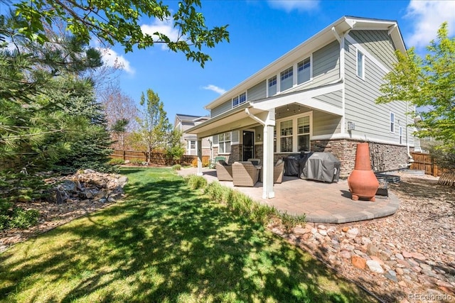 rear view of house featuring stone siding, a yard, a patio area, and a fenced backyard