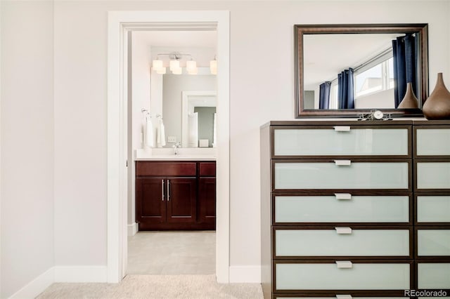 hallway with a sink, light colored carpet, and baseboards