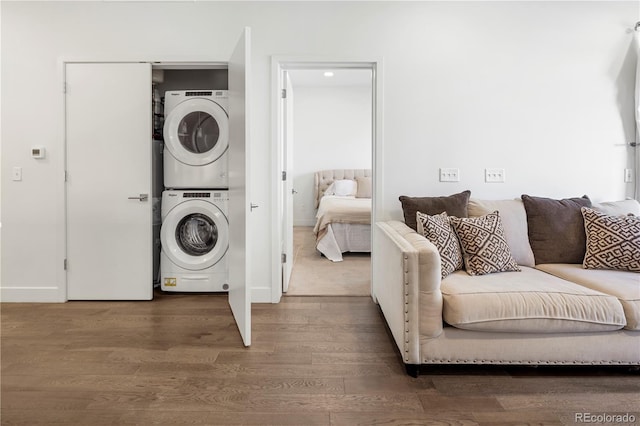 laundry area featuring baseboards, wood finished floors, stacked washer and clothes dryer, and laundry area
