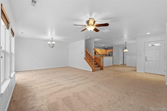 unfurnished living room with ceiling fan with notable chandelier, light carpet, and plenty of natural light