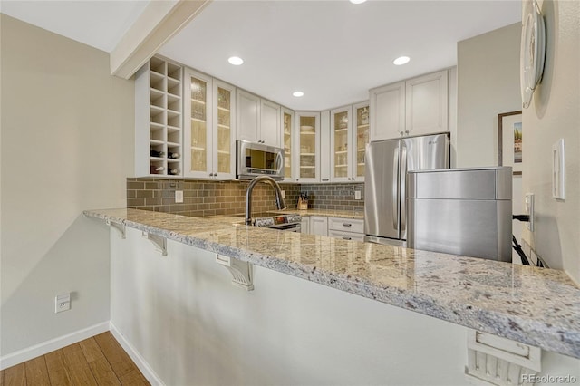 kitchen with white cabinetry, backsplash, light stone countertops, and appliances with stainless steel finishes