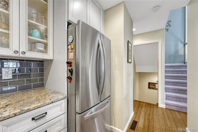 kitchen with light hardwood / wood-style flooring, stainless steel refrigerator, tasteful backsplash, light stone counters, and white cabinets