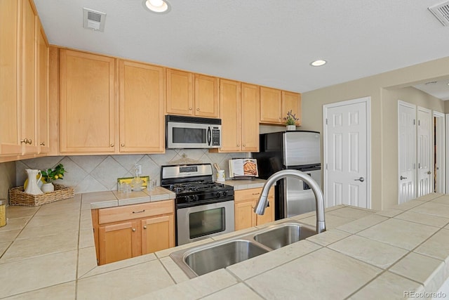 kitchen with light brown cabinetry, tile counters, stainless steel appliances, and sink