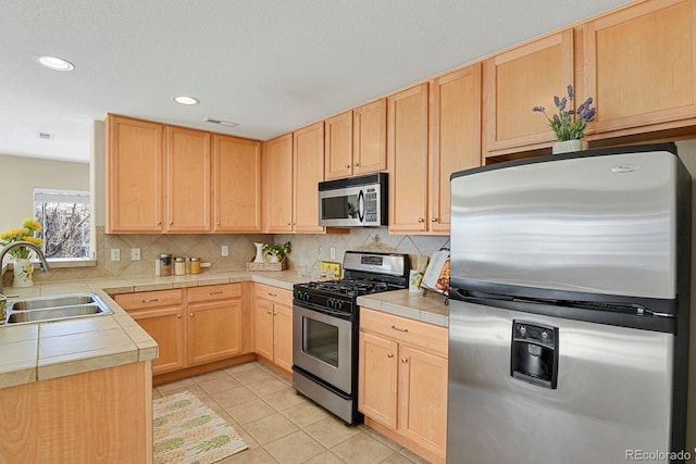 kitchen featuring tile countertops, sink, light tile patterned floors, appliances with stainless steel finishes, and tasteful backsplash