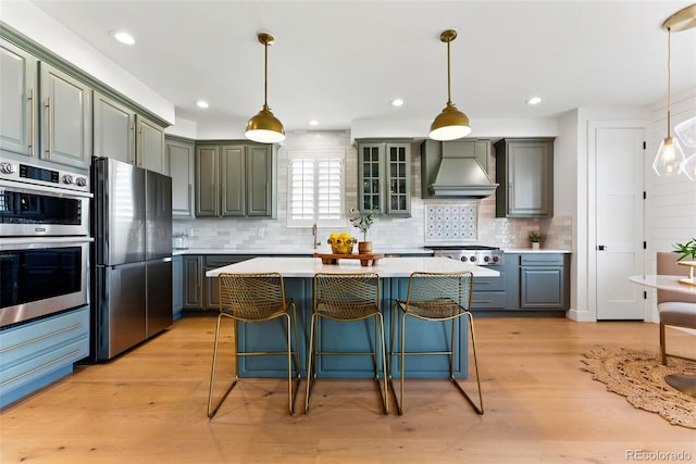 kitchen with stainless steel appliances, light wood finished floors, light countertops, and wall chimney range hood