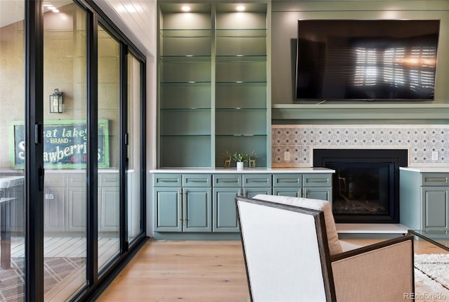 kitchen featuring a tiled fireplace, light countertops, light wood-type flooring, and green cabinets