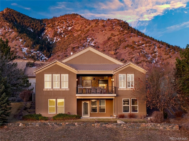 back of property featuring a tiled roof, stucco siding, a mountain view, and a balcony