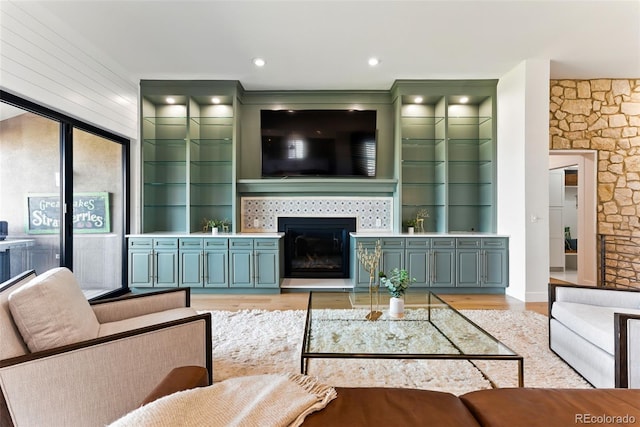 living room featuring a glass covered fireplace, built in shelves, and light wood-style floors