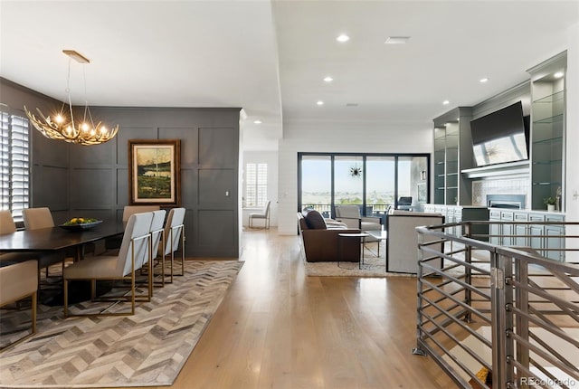 dining room with wood finished floors, recessed lighting, an inviting chandelier, crown molding, and a tile fireplace