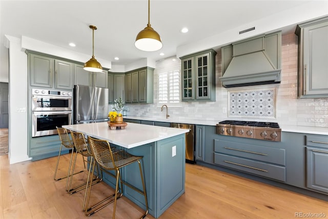 kitchen with a kitchen bar, custom range hood, light wood-style flooring, appliances with stainless steel finishes, and a sink