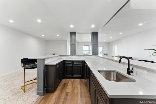 kitchen featuring a sink, recessed lighting, a breakfast bar area, light wood finished floors, and light countertops