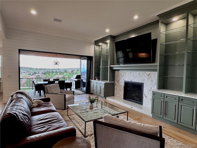 living room featuring a tiled fireplace, plenty of natural light, light wood-type flooring, and wood walls