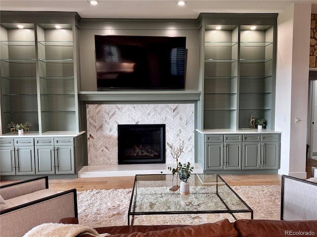 living area with a tiled fireplace, built in features, ornamental molding, and light wood-style flooring