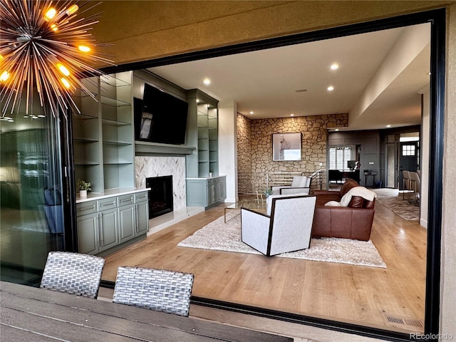 living area featuring an inviting chandelier, light wood-style floors, built in shelves, recessed lighting, and a high end fireplace