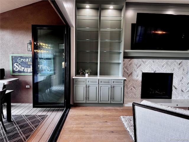 bar featuring light wood-style floors, a tiled fireplace, and vaulted ceiling