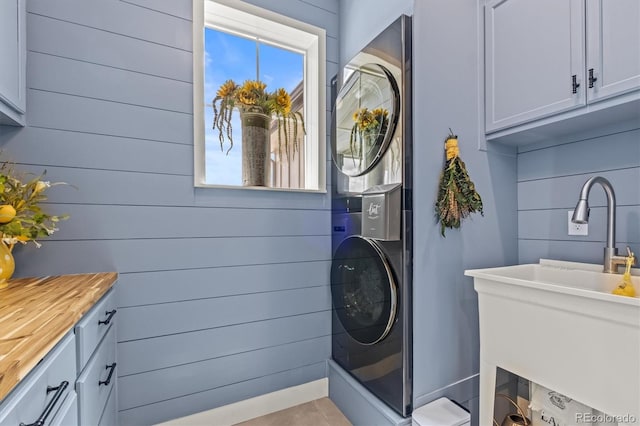 laundry room with sink, stacked washing maching and dryer, cabinets, and wooden walls