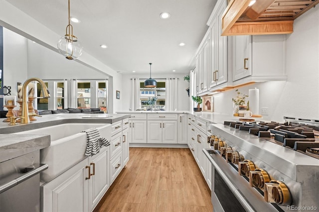 kitchen with white cabinets, appliances with stainless steel finishes, light wood-type flooring, sink, and decorative light fixtures