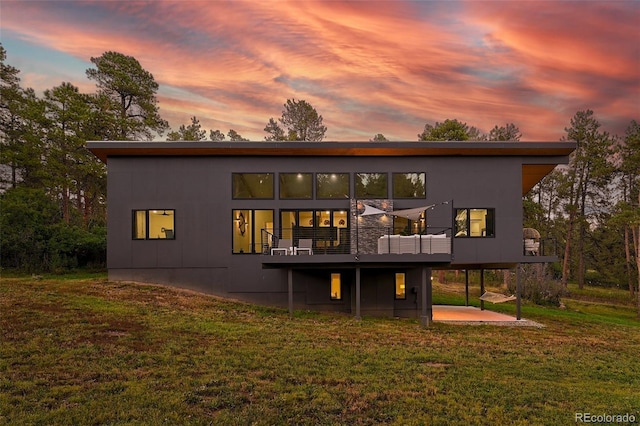 back of property at dusk with a wooden deck, a lawn, and a patio